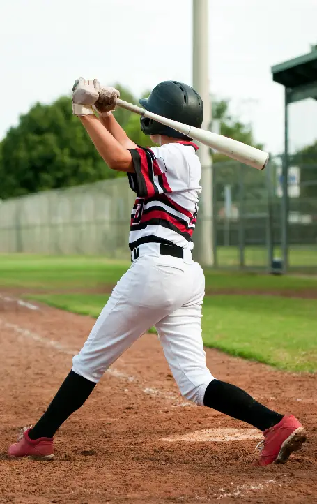 h3-body A young baseball player swings a bat, wearing a black helmet, a red and white jersey, and black pants on a field